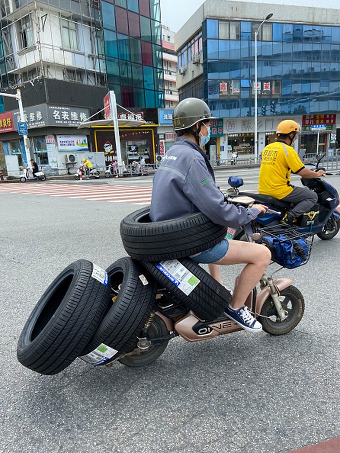 HUAI'AN, CHINA - JULY 26, 2022 - A female electric driver drives slowly with four car tires and a car tire around her waist on a street in Huai 'an, East China's Jiangsu Province, China, July 26, 2022. (Photo credit should read CFOTO/Future Publishing via Getty Images)