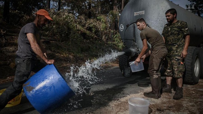 Saat Para Pemburu di Prancis Berbagi Air untuk Hewan di Hutan yang Terbakar French hunters carry a debris to be used for a water point for wild animals on July 23, 2022 in a forest ravaged by a wildfire near Pyla sur Mer in Gironde, southwestern France. (Photo by Philippe LOPEZ / AFP) (Photo by PHILIPPE LOPEZ/AFP via Getty Images)