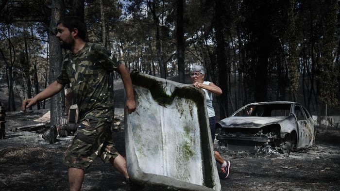 French hunters carry a debris to be used for a water point for wild animals on July 23, 2022 in a forest ravaged by a wildfire near Pyla sur Mer in Gironde, southwestern France. (Photo by Philippe LOPEZ / AFP) (Photo by PHILIPPE LOPEZ/AFP via Getty Images)