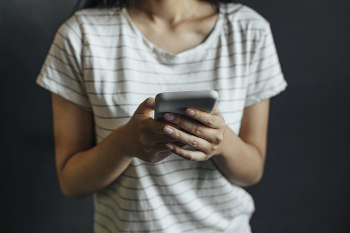 An unrecognizable woman dressed in a white T-shirt with black stripes texting on her smartphone.