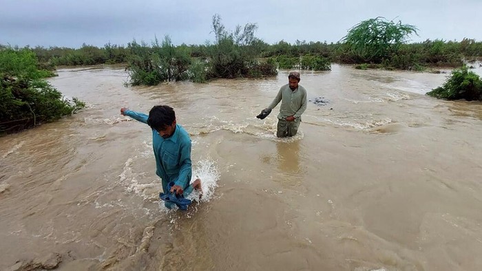 Villagers cross a flooded area to move into higher place after heavy rains, in Lasbella, a district in Pakistan's southwest Baluchistan province, Tuesday, July 26, 2022. Officials say, on Wednesday, rescuers backed by troops are using boats and helicopters to evacuate hundreds of marooned people from Pakistan's southwest, where floods triggered by rains have killed 104 people since last month. (AP Photo/Hamdan Khan)