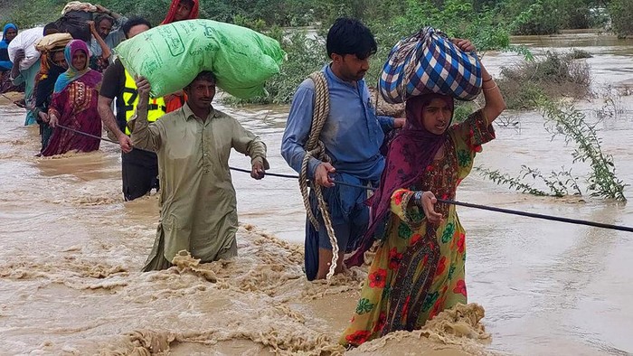 Villagers cross a flooded area to move into higher place after heavy rains, in Lasbella, a district in Pakistans southwest Baluchistan province, Tuesday, July 26, 2022.  Officials say, on Wednesday, rescuers backed by troops are using boats and helicopters to evacuate hundreds of marooned people from Pakistans southwest, where floods triggered by rains have killed 104 people since last month.  (AP Photo/Hamdan Khan)