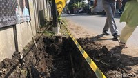 Galian parit yang belum selesai diberi pita kuning memanjang. Nampak penggalian parit terhalang tiang utilitas.