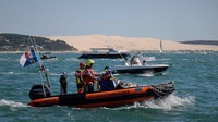 Sebuah perahu motor berlayar di lautan dengan latar belakang Dune du Pilat.