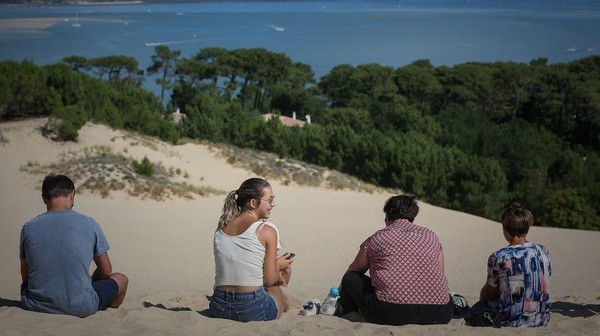 Orang-orang duduk santai di Dune du Pilat sambil menikmati pemandangan.