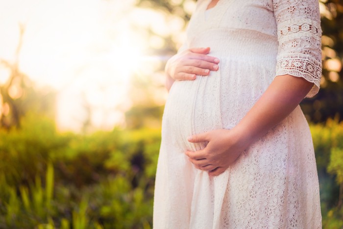 Pregnant woman feeling happy with new life at garden home while take care of her child. The young expecting mother holding baby in pregnant belly. Maternity prenatal care and woman pregnancy concept.