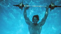 Aksi Arnold Schwarzenegger mengangkat barbel di dasar kolam di Los Angeles, California, pada 1977. Michael Ochs/Getty Images.