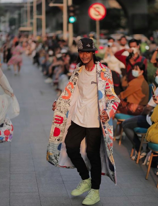 Inilah aksi Bonge menjadi model di fashion show resmi tersebut. Bonge mengenakan coat panjang bermotif dan sepatu warna hijau neon. Dia masih mempertahankan style ikoniknya yakni topi yang selalu dipakainya. Foto: dok. Instagram/Calla The Label