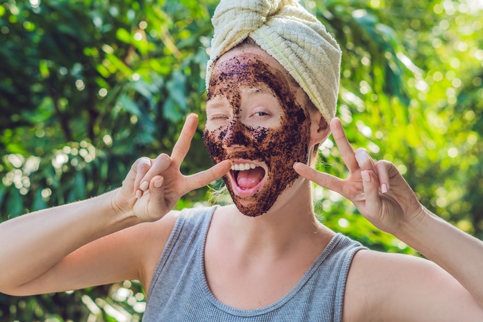 Face Skin Scrub. Portrait Of Sexy Smiling Female Model Applying Natural Coffee Mask, Face Scrub On Facial Skin. Closeup Of Beautiful Happy Woman With Face Covered With Beauty Product. High Resolution.