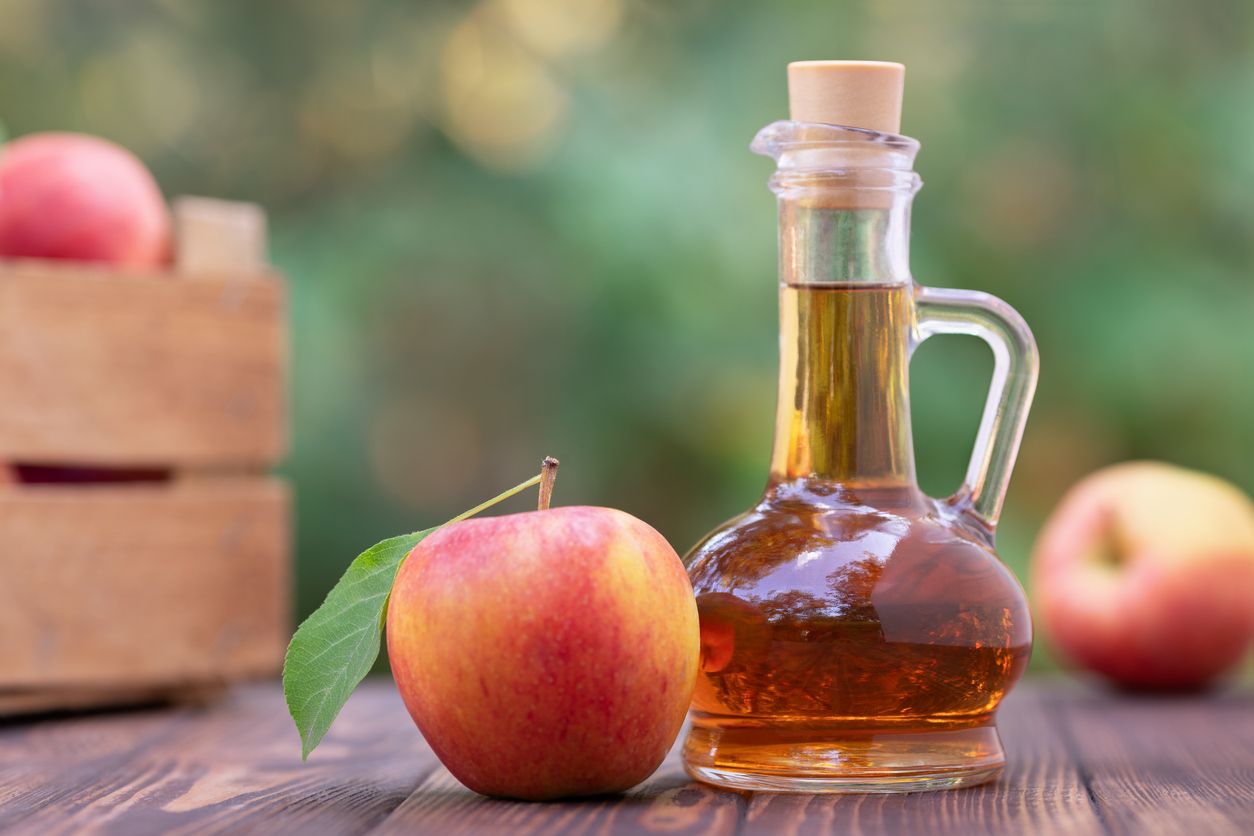apple vinegar in glass pitcher and ripe fresh apples on wooden table outdoors