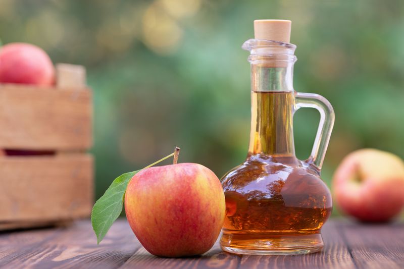 apple vinegar in glass pitcher and ripe fresh apples on wooden table outdoors