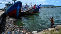 Kapal bersandar di Pelabuhan Banda Aceh yang tercoreng oleh sampah plastik dan limbah berminyak. Di dekatnya pemancing melempar kail untuk mencari ikan.