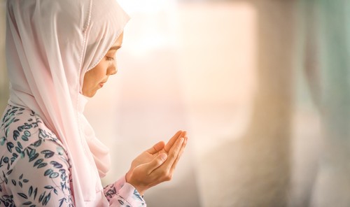 Young beautiful muslim women open palm, peaceful praying in mosque.