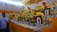 Seorang pria berdiri di dekat foto-foto orang yang jenazahnya akan dikremasi dalam upacara kremasi massal tradisional yang disebut ngaben. Jenazah yang sebelumnya terkubur digali dan ditempatkan di kuil sementara sebelum dikremasi.