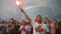 Ratusan warga Polandia berdiri di persimpangan utama kota sambil memegang bendera nasional dan suar.