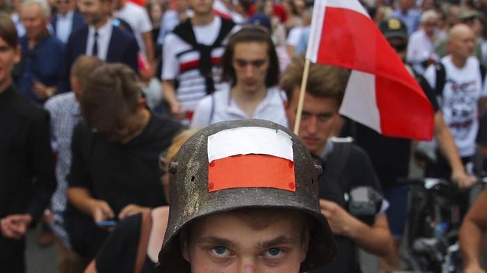 People stand on the citys main intersection holding national flags and flares to observe a minute of silence for the fighters and victims of the 1944 Warsaw Uprising against the Nazi German occupiers, in Warsaw, Poland, Monday Aug. 1, 2022. Poles are marking the 78th anniversary of the Warsaw Uprising, a doomed revolt against Nazi German forces during World War II. (AP Photo/Michal Dyjuk)