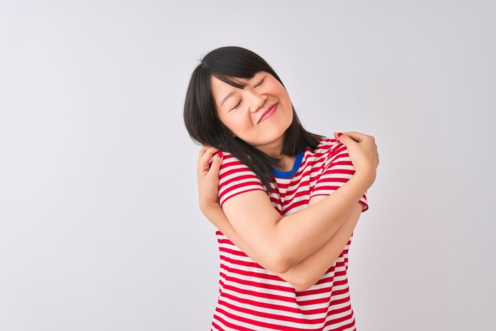 Young beautiful chinese woman wearing red striped t-shirt over isolated white background Hugging oneself happy and positive, smiling confident. Self love and self care