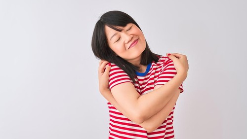 Young beautiful chinese woman wearing red striped t-shirt over isolated white background Hugging oneself happy and positive, smiling confident. Self love and self care