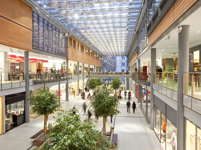 Image taken inside a shopping mall. There are lots of people walking around going to stores, buying things and consuming food and beverages. There are two floors with shops and boutiques. The ceiling is glass. The architecture is very modern and new and the general feel of the images is bright, clean, safe and positive.