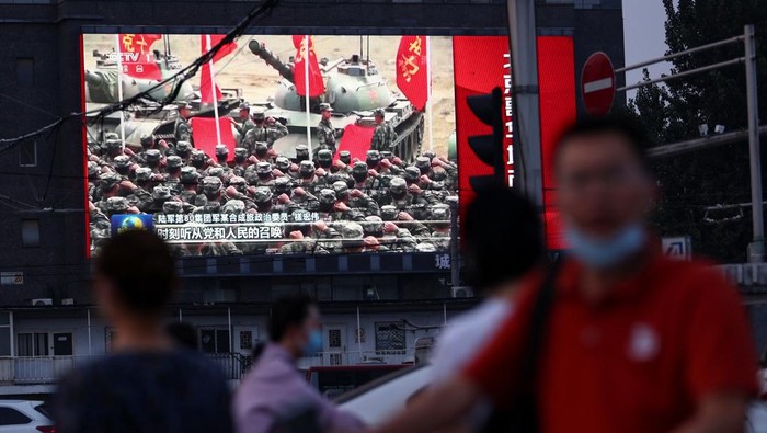 Pedestrians walk past a screen showing footage of Chinese Peoples Liberation Army (PLA) ships during an evening news programme, in Beijing, China August 2, 2022. REUTERS/Tingshu Wang