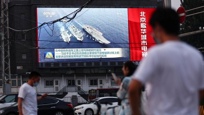Pedestrians walk past a screen showing footage of Chinese People's Liberation Army (PLA) ships during an evening news programme, in Beijing, China August 2, 2022. REUTERS/Tingshu Wang