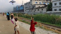 Anak-anak bermain layangan di daerah yang tercemar udara saat asap mengepul dari pabrik penggilingan ulang di Dhaka, Bangladesh, Rabu (03/08/2022).