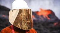 Petugas memakai alat pelindung saat berdiri di dekat lava pijar.