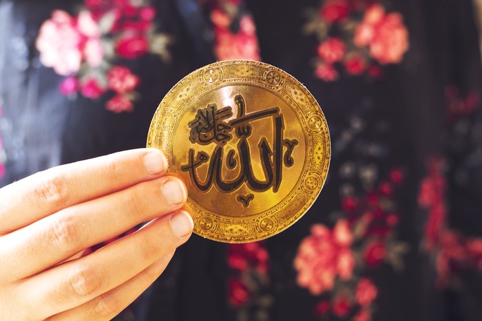 muslim woman holding a golden paper  with Arabic calligraphy of Allah (Islamic God)