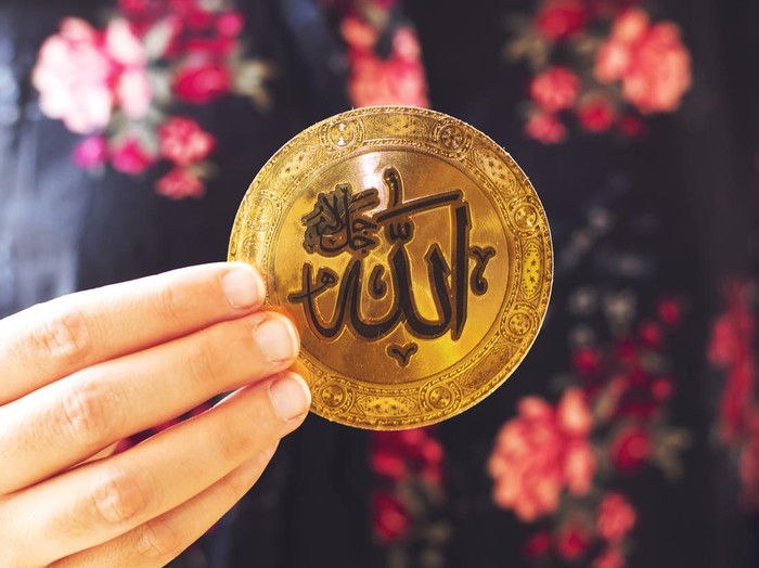 muslim woman holding a golden paper  with Arabic calligraphy of Allah (Islamic God)