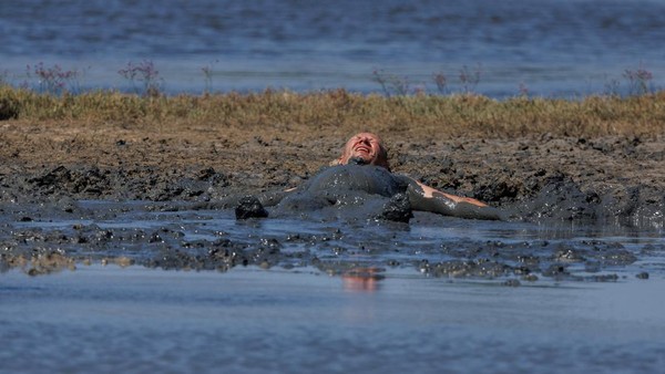 Seorang pria terlihat berlumuran lumpur di Pantai Queens di Kota Nin, Kroasia, Rabu, (3/8/2022).