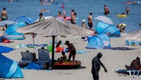 Seorang wisatawan yang berselimut lumpur berjalan di Pantai Queen.