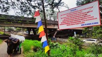 Warga melintas di sekitar spanduk bertuliskan pesan buruk kepada para pembuang sampah sembarangan. 