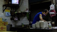 Pemilik restoran sedang menyajikan makanan. Terlihat televisi yang berada di atas dapur tesebut menayangkan siaran berita live tentang China melakukan latihan militer.
