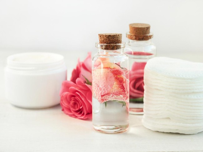 Glass bottle with attar bubbles and rose petals, cotton pads. Healing homemade skincare moisture toni