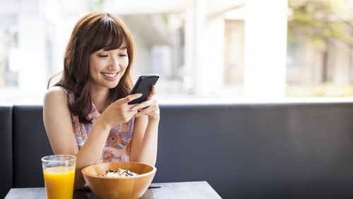 Pretty, casually dressed asian girl is having lunch in a cafe and using her smartphone for social media browsing. Image contains copy space.