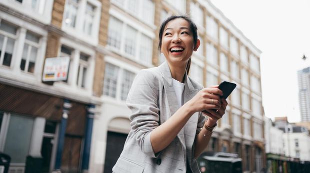 Asian business woman looking far away while using her smartphone on the street of London.
