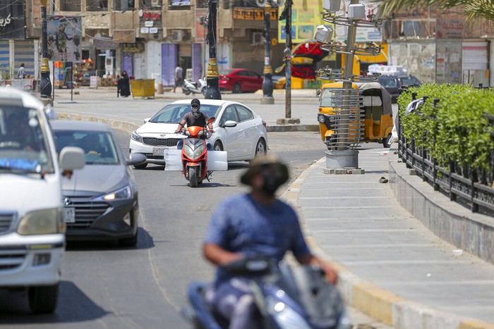 People navigate a street with a poster of Shiite religious leaders Mohammed Sadiq al-Sadr, right, and his relative, Mohammed Baqir al-Sadr, left, displayed in Baghdad's Shiite enclave of Sadr City, in Baghdad, Iraq, Thursday, Aug. 4, 2022.  Residents of the impoverished suburb say they they support an influential Shiite cleric who called on thousands of his followers to storm Iraq's parliament.  (AP Photo/Anmar Khalil)