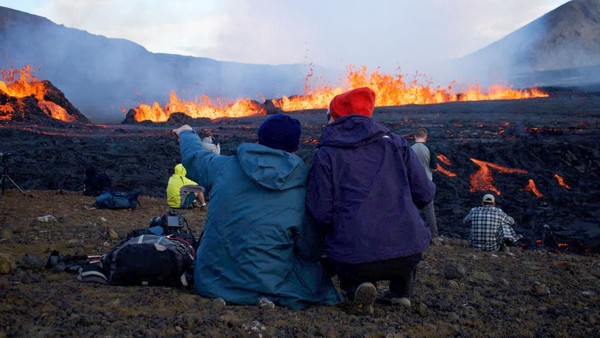 Orang-orang melihat lava yang meletus dan mengalir di lokasi gunung berapi yang baru meletus di Grindavik, Islandia. (Jeremie Richard/AFP/Getty Images)