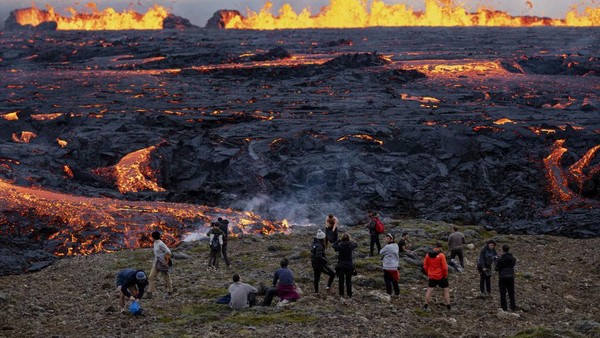 Penampakan gunung berapi saat lava mengalir melalui celah baru setelah letusan gunung berapi di lembah Meradalir. Wisatawan nampak asyik menyaksikan fenomena alam tersebut. Tidak sedikit dari mereka mengabadikannya dengan ponsel. (Ernir Eyjolfsson/Anadolu Agency/Getty Images)