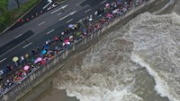 Beberapa warga terlihat membawa payung demi menghindari gelombang pasang yang menyembur hingga tepi sungai.