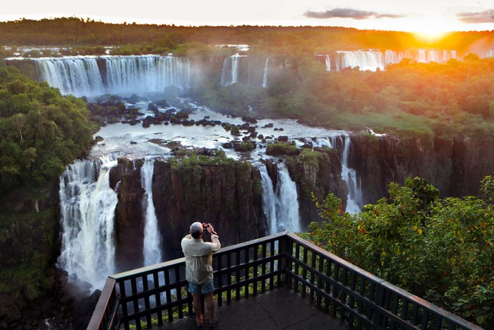 IGUACU, BRAZIL - APRIL 8: Tourists enjoy Brazilian Caipirinha cocktails, made with Cachaca, fruit and sugar,  in front of the evening panoramic view of the Argentinian side of the waterfalls on April 8, 2019 in the Iguaçu National Park, Brazil. The falls, which straddle the border of Argentina and Brazil, are known in Spanish as Cataratas del Iguazú and in Portuguese as Cataratas do Iguaçu. They are the largest waterfall system in the world made up of 275 individual drops stretching 2.7 kilometers wide and up to 82 meters in height, and were chosen in 2011 as one of the  New Seven Wonders of Nature. The Argentinian and Brazilian national parks which protect the falls host millions of tourists each year while protecting the environment by limiting vehicle access and using ecological transportation systems within the parks. (Photo by David Silverman/Getty Images)