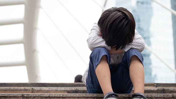 Homeless Asian child sitting alone on the stairway in the street. Poor, sad, scared and alone.