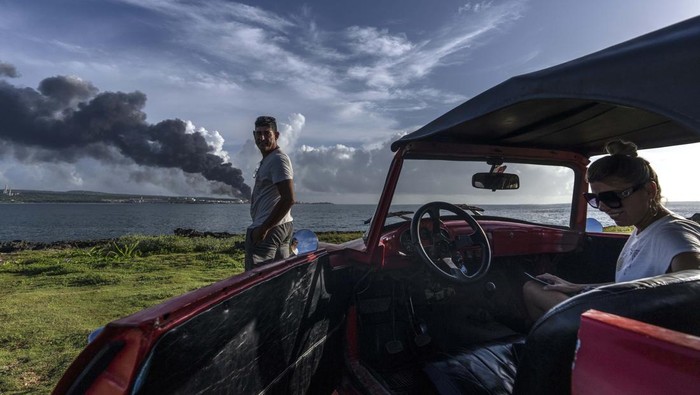 People watch a huge plume of smoke rise from the Matanzas supertanker base, as firefighters work to douse a fire that started during a thunderstorm the night before, in Matanzas, Cuba, Sunday, Aug. 7, 2022. Cuban authorities say lightning struck a crude oil storage tank at the base, sparking a fire that sparked four explosions that injured more than 121 people, one person dead and 17 missing. (AP Photo/Ramon Espinosa)