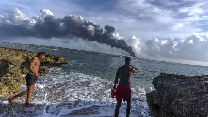 Kebakaran Hebat di Depot Minyak Kuba jadi Tontonan People watch a huge plume of smoke rise from the Matanzas supertanker base, as firefighters work to douse a fire that started during a thunderstorm the night before, in Matanzas, Cuba, Sunday, Aug. 7, 2022. Cuban authorities say lightning struck a crude oil storage tank at the base, sparking a fire that sparked four explosions that injured more than 121 people, one person dead and 17 missing. (AP Photo/Ramon Espinosa)