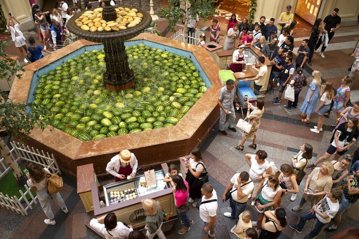 Russia Daily Life A man help his child to look at a fountain decorated with Astrakhan watermelons and Asian melons inside the GUM department store in Moscow, Russia, Sunday, Aug. 7, 2022. Markets selling Astrakhan watermelons and Asian melons traditionally open in Moscow in August. (AP Photo/Alexander Zemlianichenko)