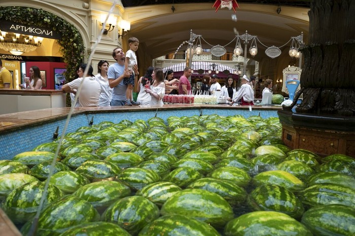 A man help his child to look at a fountain decorated with Astrakhan watermelons and Asian melons inside the GUM department store in Moscow, Russia, Sunday, Aug. 7, 2022. Markets selling Astrakhan watermelons and Asian melons traditionally open in Moscow in August. (AP Photo/Alexander Zemlianichenko)