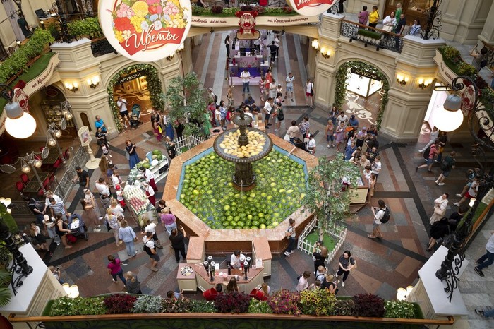 A man help his child to look at a fountain decorated with Astrakhan watermelons and Asian melons inside the GUM department store in Moscow, Russia, Sunday, Aug. 7, 2022. Markets selling Astrakhan watermelons and Asian melons traditionally open in Moscow in August. (AP Photo/Alexander Zemlianichenko)