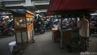 Gerobak pedagang diparkir di jalan aspal sambil melayani pembeli. Meski kemacetan terjadi setiap pagi, para pedagang kaki lima ini tetap berjualan di bahu jalan. Atau sebaliknya, para PKL memanfaatkan situasi macet untuk berjualan.