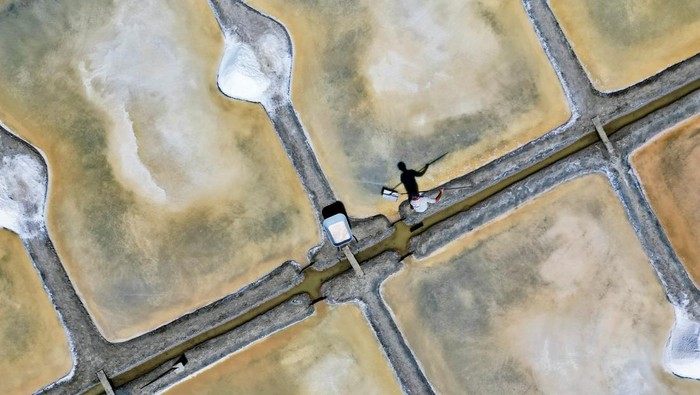 French salt maker Francois Durand harvests sea salt from a salt pan in Le Pouliguen, west France, August 5, 2022. The country’s record heatwave has seen salt yields nearly double this season as sunlight and light winds have driven the evaporation of seawater that’s let into the pans at high tides.  REUTERS/Yann Tessier