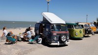 Banyak VW Kombi yang diparkir di tepi pantai dengan penampilan yang unik dan warna-warni.